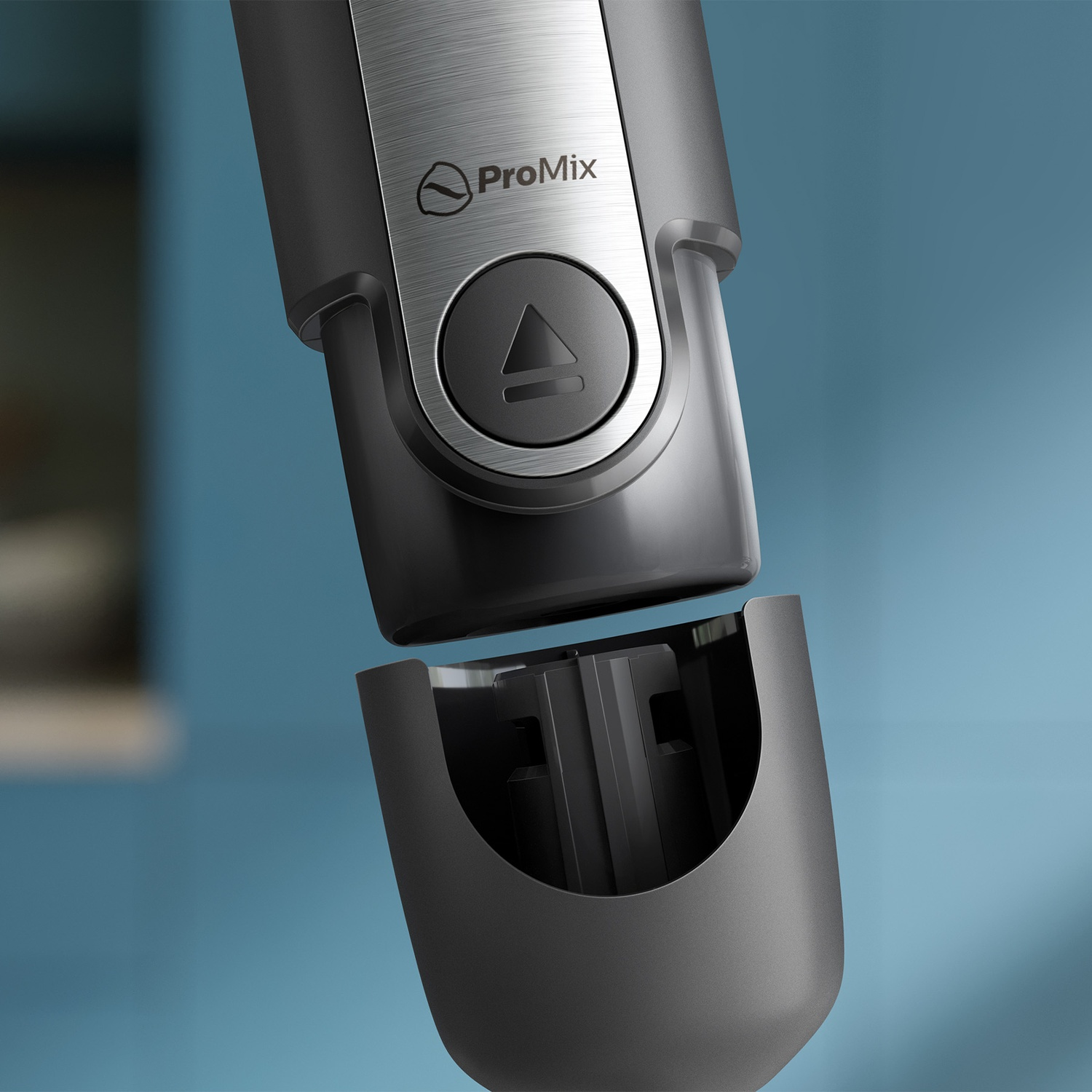 Close-up of a grey ProMix hand blender with a detachable attachment against a blue background.