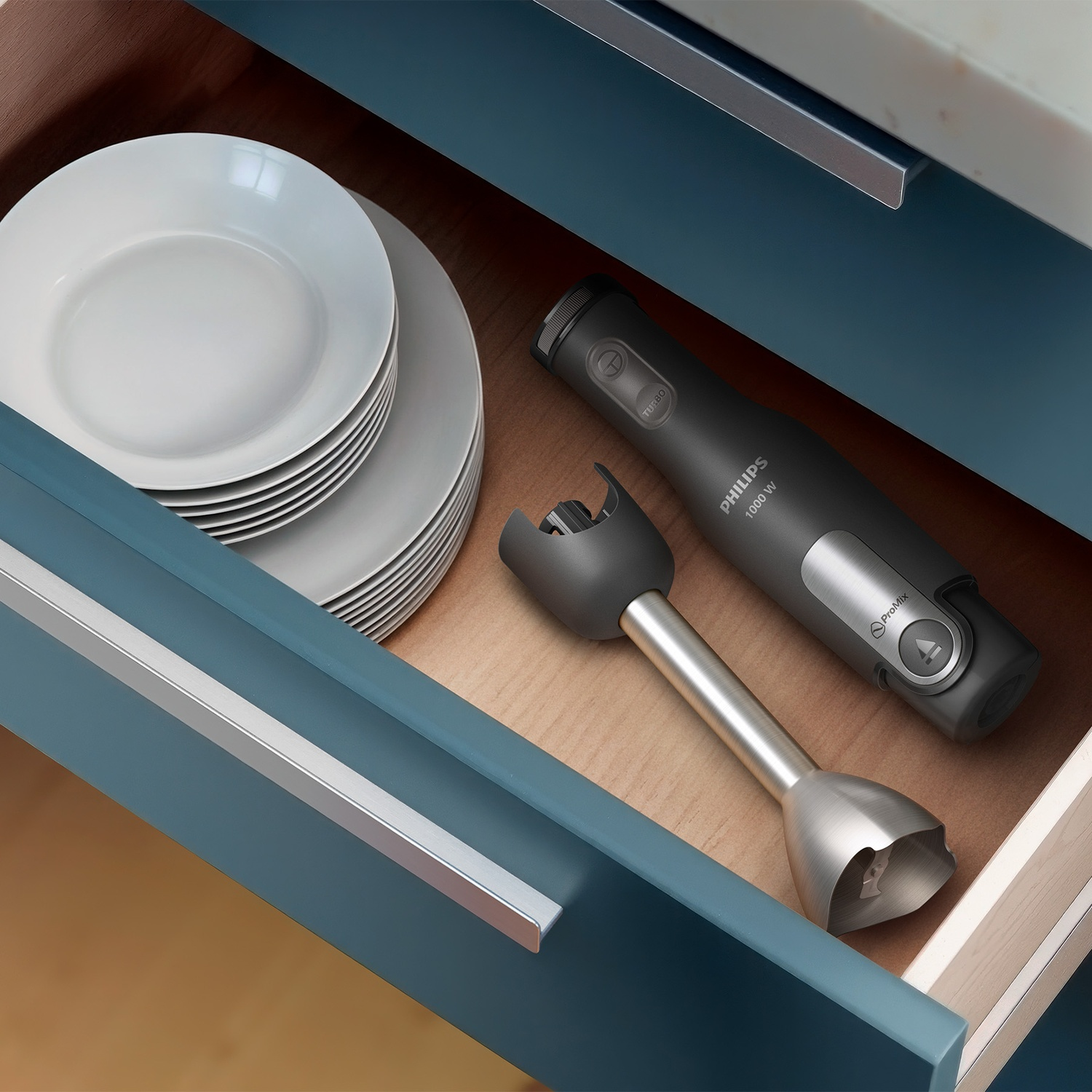 An open blue kitchen drawer contains a stack of white plates and a disassembled black and silver hand blender.