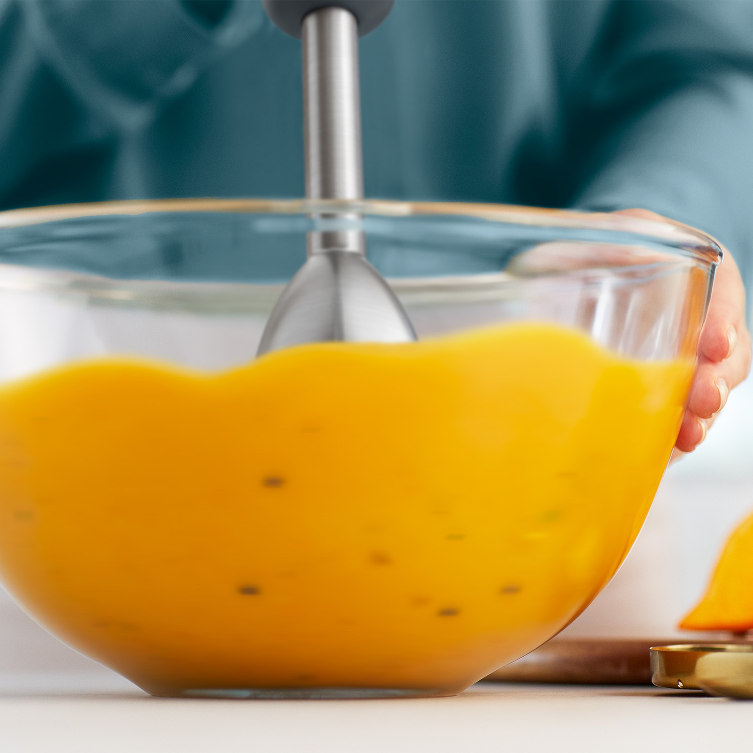 An immersion blender mixes yellow batter inside a large glass bowl.