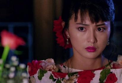 Eine asiatische Frau mit dunklem Haar, rotem Lippenstift und einem Kleid mit Rosenmuster blickt besorgt nach links.