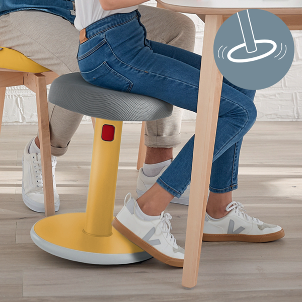 Eine Person sitzt auf einem gelben, beweglichen Hocker an einem Holztisch.