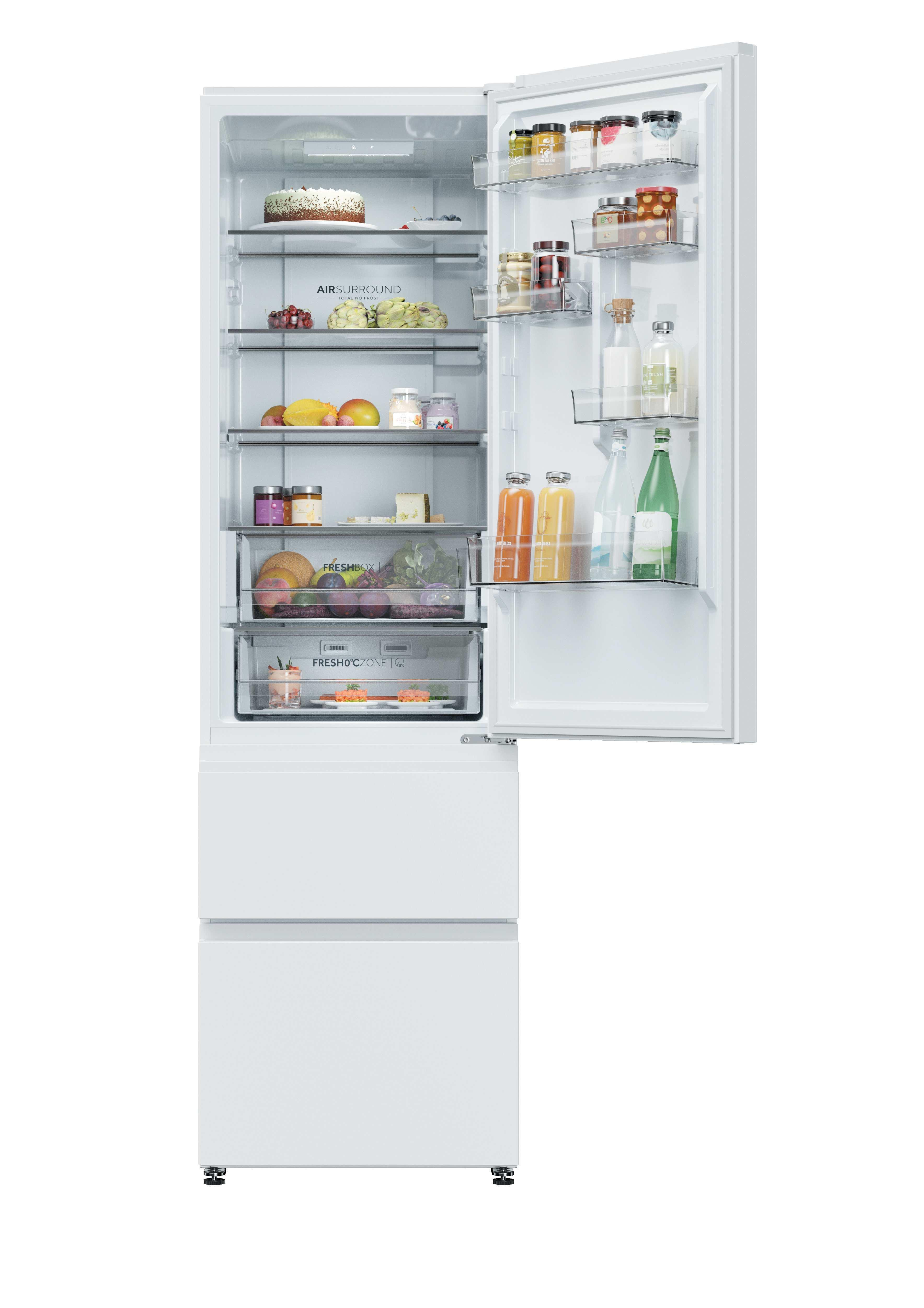 Un refrigerador blanco abierto lleno de frutas frescas, bebidas y alimentos en estantes y cajones.