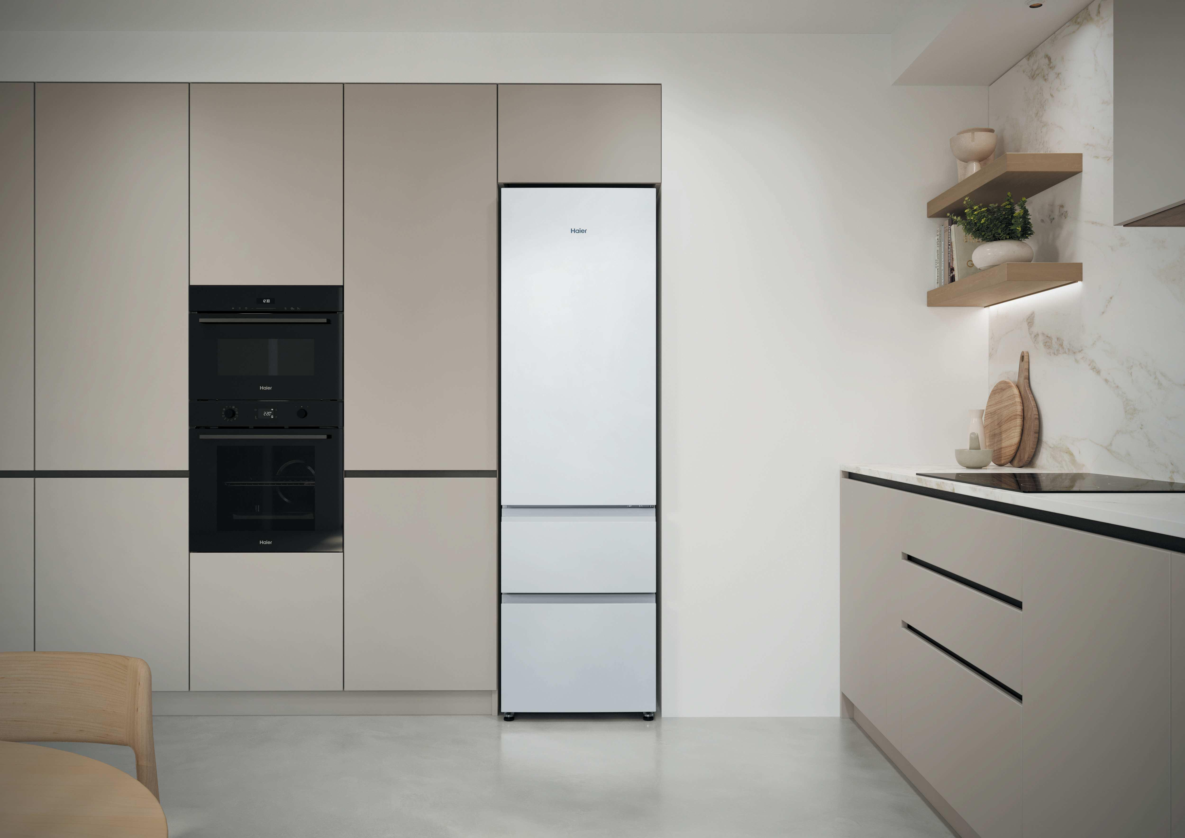 Moderna cocina con frigorífico blanco integrado, hornos oscuros, armarios beiges y estantes de madera.
