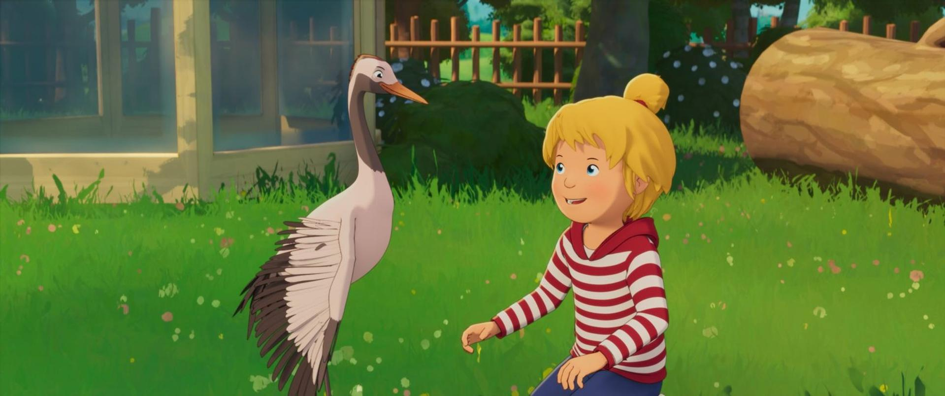 Ein blondes Mädchen im rot-weiß gestreiften Pullover kniet im Gras neben einem großen weißen Vogel.