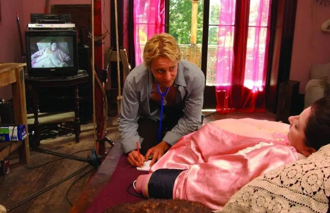 Ein blondes Ärzt mit Stethoskop schreibt Notizen am Bett einer Patientin in rosa.