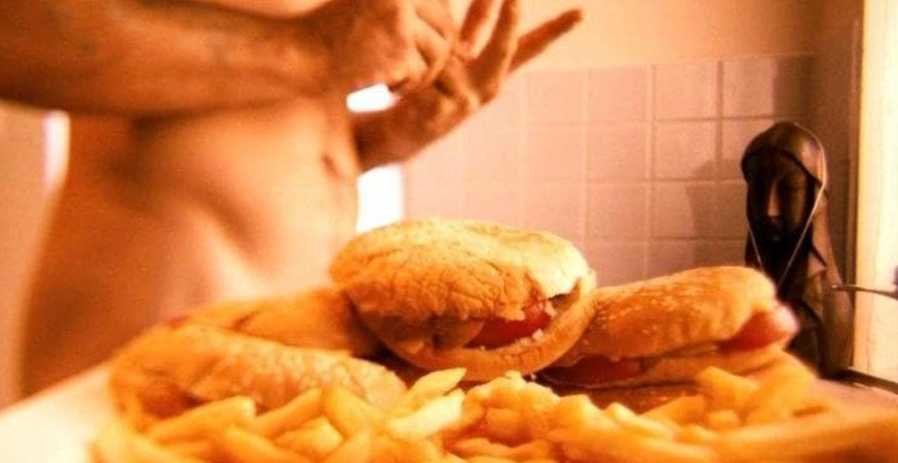 Unscharfer Hintergrund zeigt eine nackte Person vor Sandwiches und Pommes. Rechts steht eine kleine Figur.