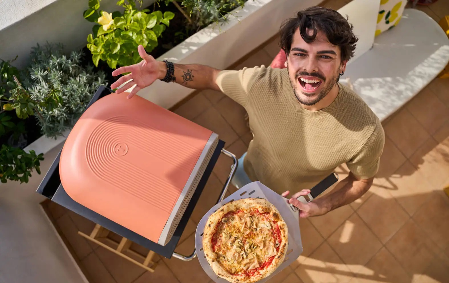 Szczęśliwy mężczyzna dumnie prezentuje świeżo upieczoną pizzę obok różowego pieca.