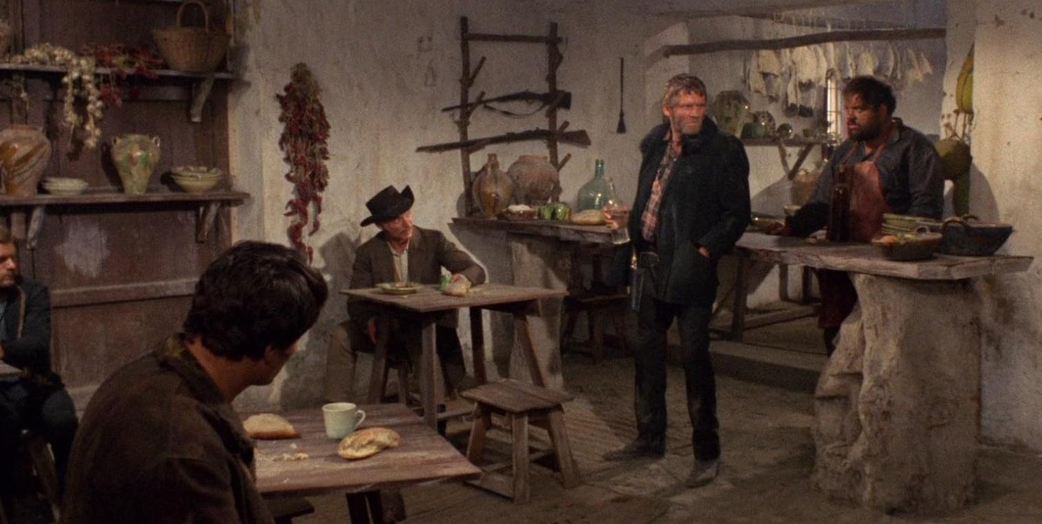 Männer versammeln sich in einer rustikalen Taverne mit Steinwänden, Holztischen und Regalen voller Krüge und Vorräte.