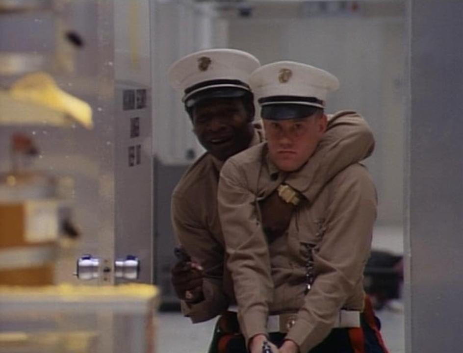 Zwei Marinesoldaten in Uniform halten gemeinsam eine Pistole in einem Flur.