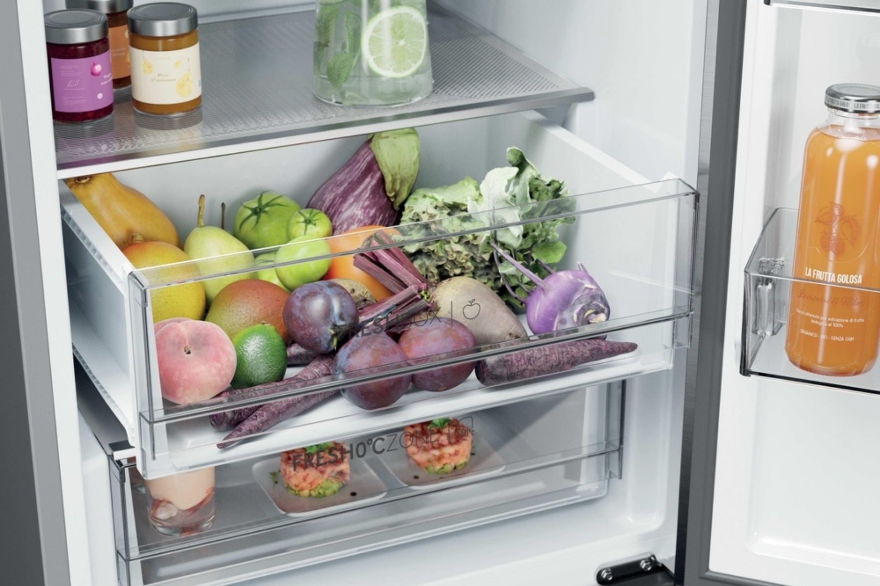 La puerta abierta del refrigerador muestra un cajón lleno de frutas, verduras y bebidas frescas.