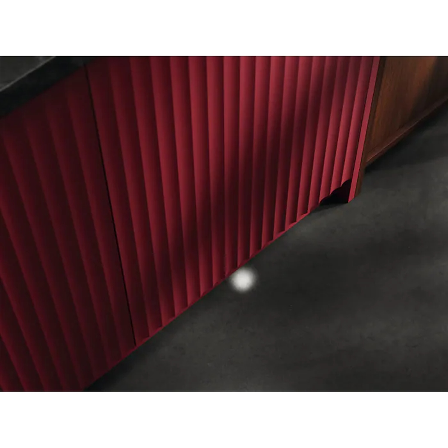 Red ribbed kitchen cabinet base with a warm light spot on the dark floor.