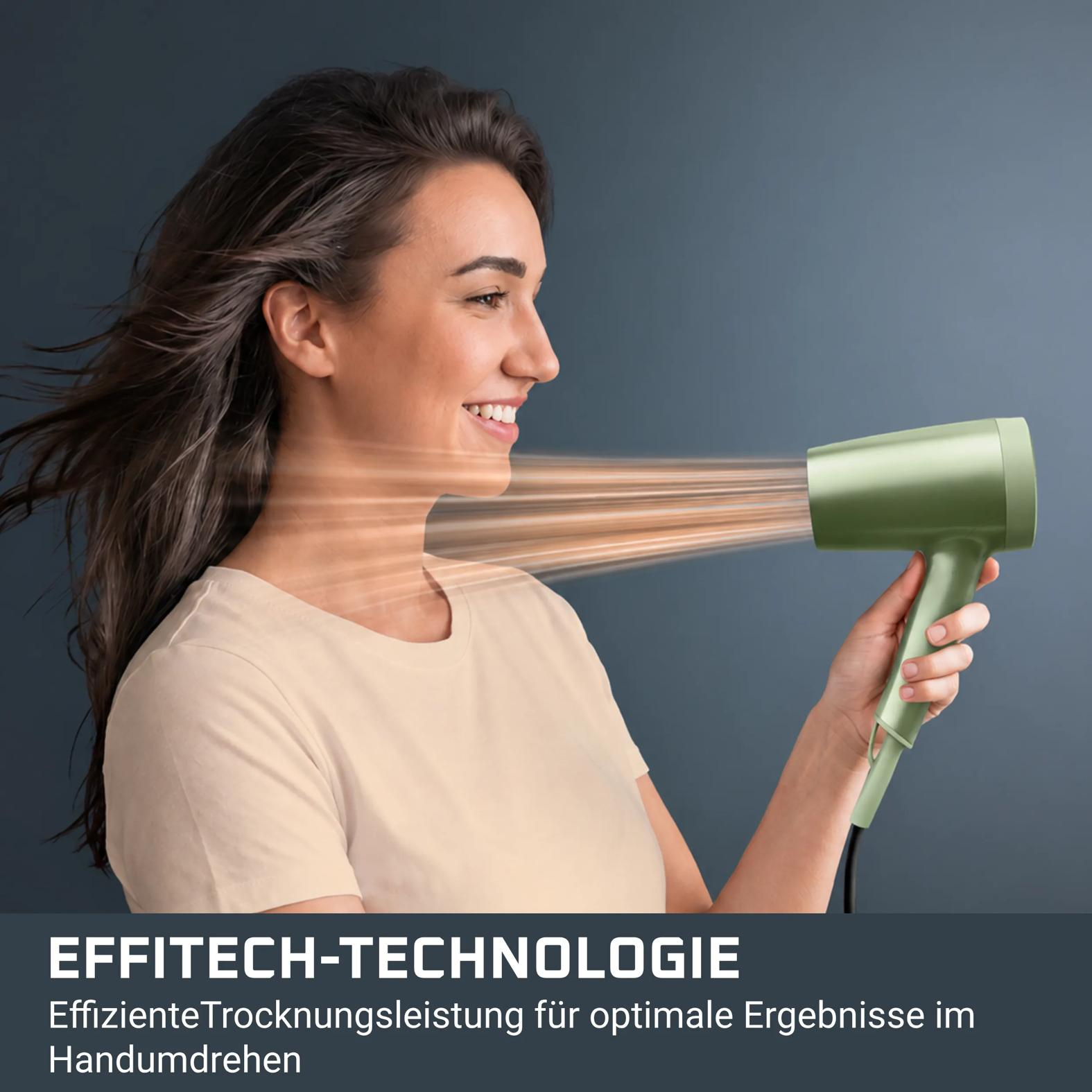 Eine lächelnde Frau hält einen grünen Föhn vor dunklem Hintergrund, während Luft ihr Haar bewegt.
