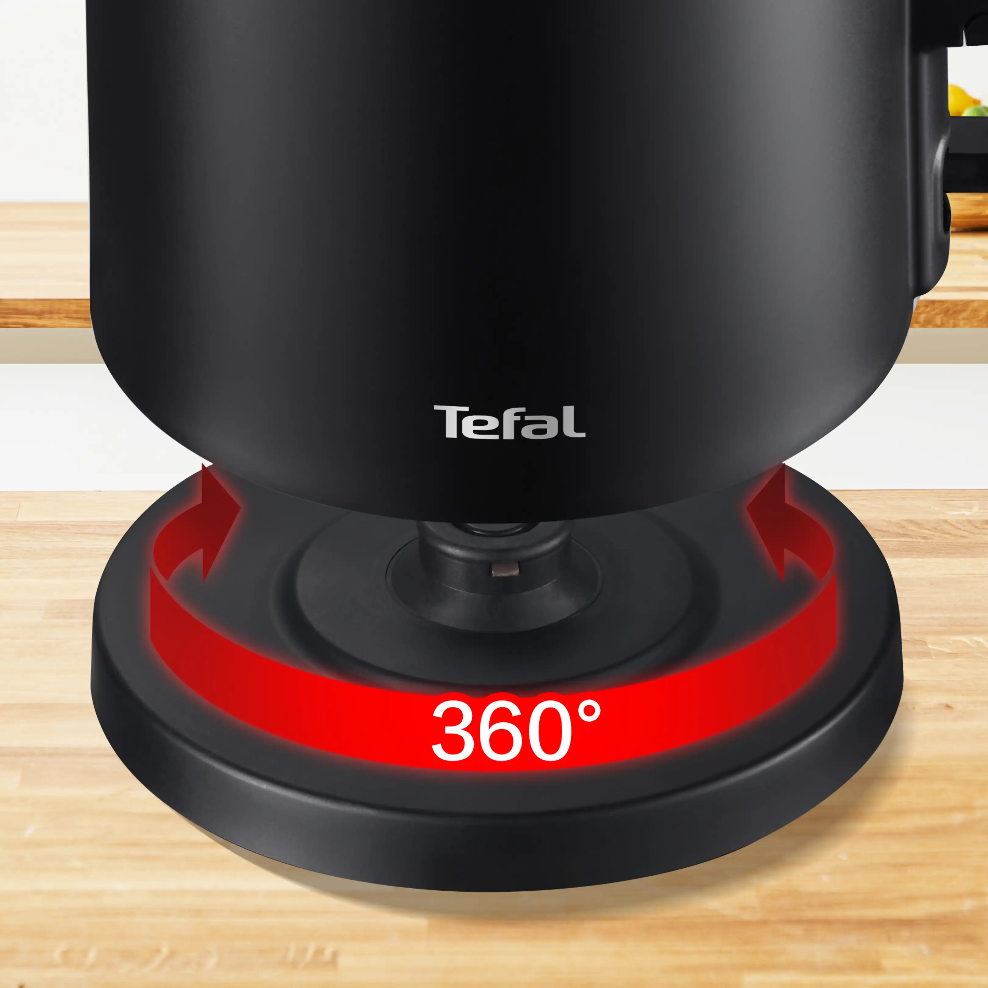 Un bollitore elettrico Tefal nero su una base girevole a 360 gradi con una freccia rossa, su un piano di lavoro in legno.
