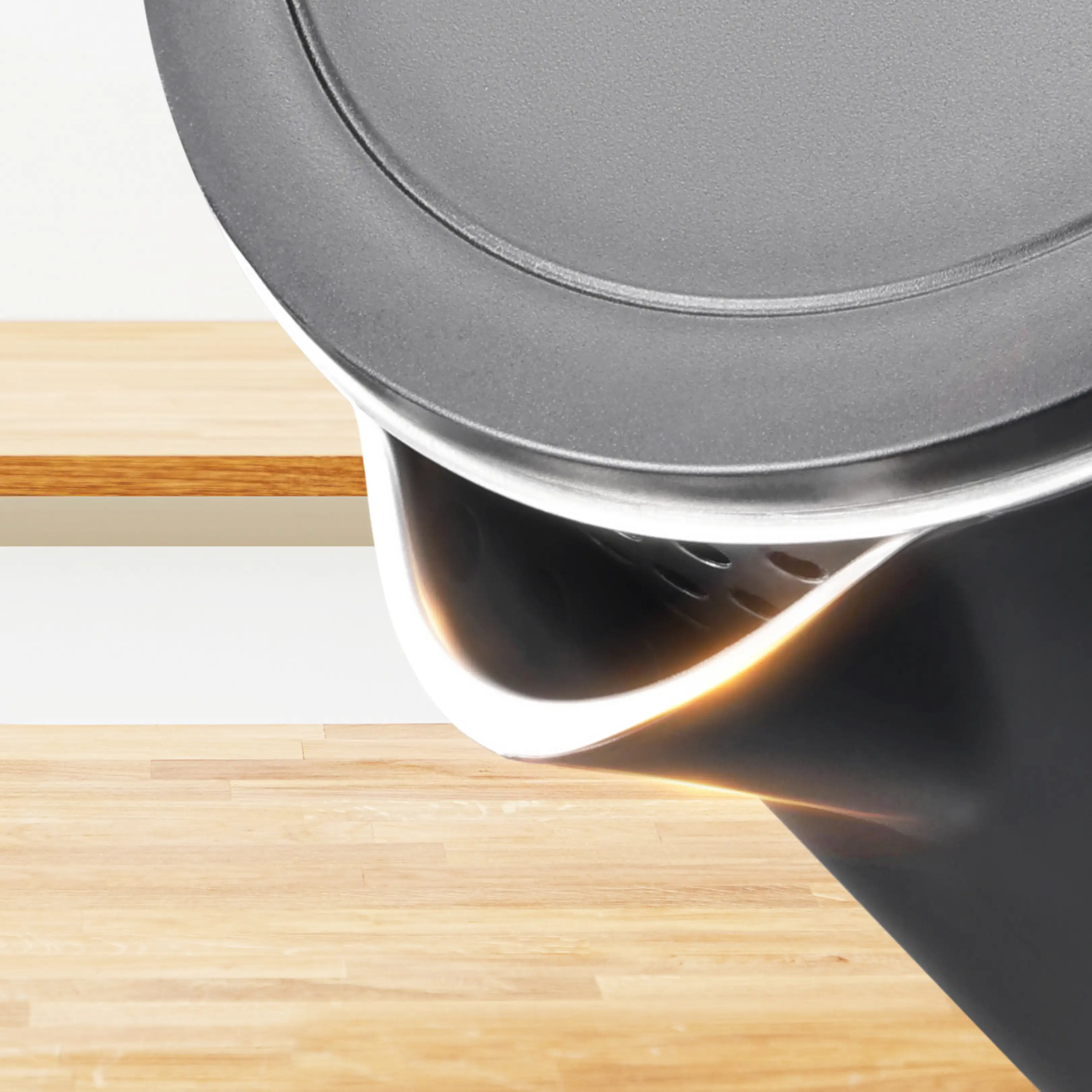 Primo piano di un bollitore scuro con coperchio e beccuccio, su sfondo in legno chiaro.