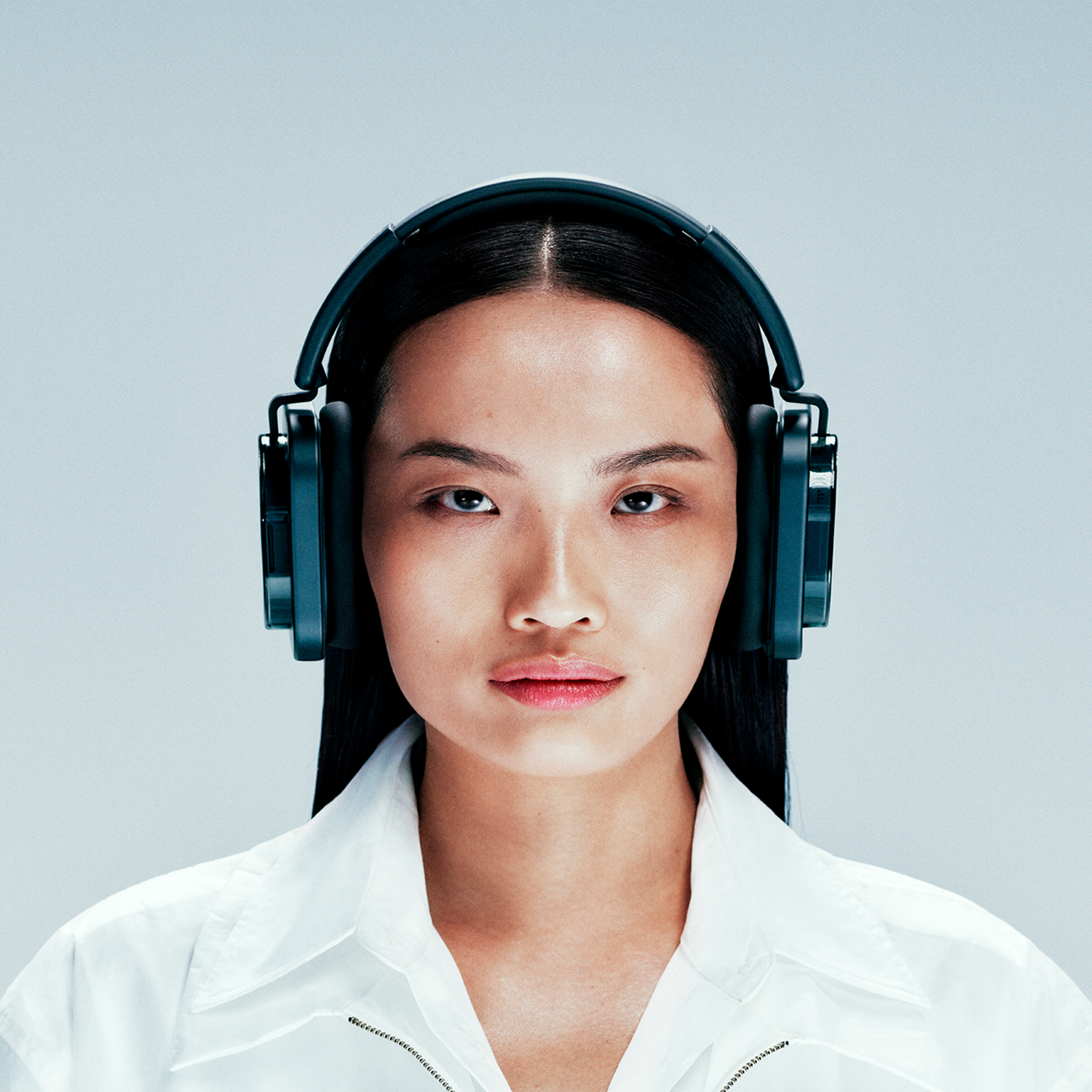 Frontalportrait einer asiatischen Frau mit langen dunklen Haaren, weißen Oberteil und großen grauen Kopfhörern.