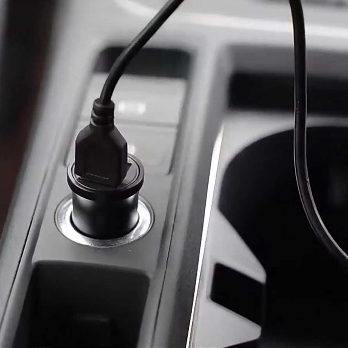Fekete USB autós töltő bedugva az autó középkonzoljának aljzatába.