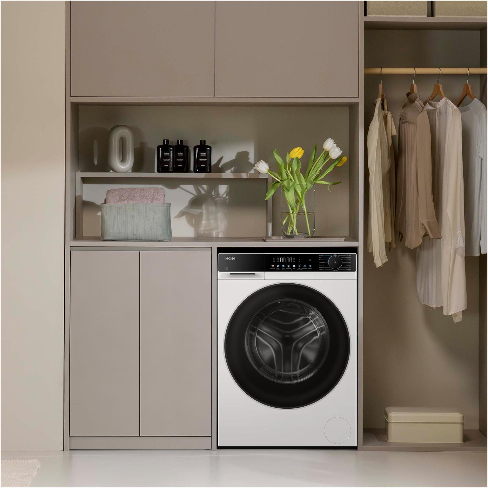 Eine weiße Waschmaschine in einem modernen Hauswirtschaftsraum mit Regalen, Kleidung und gelben Blumen.