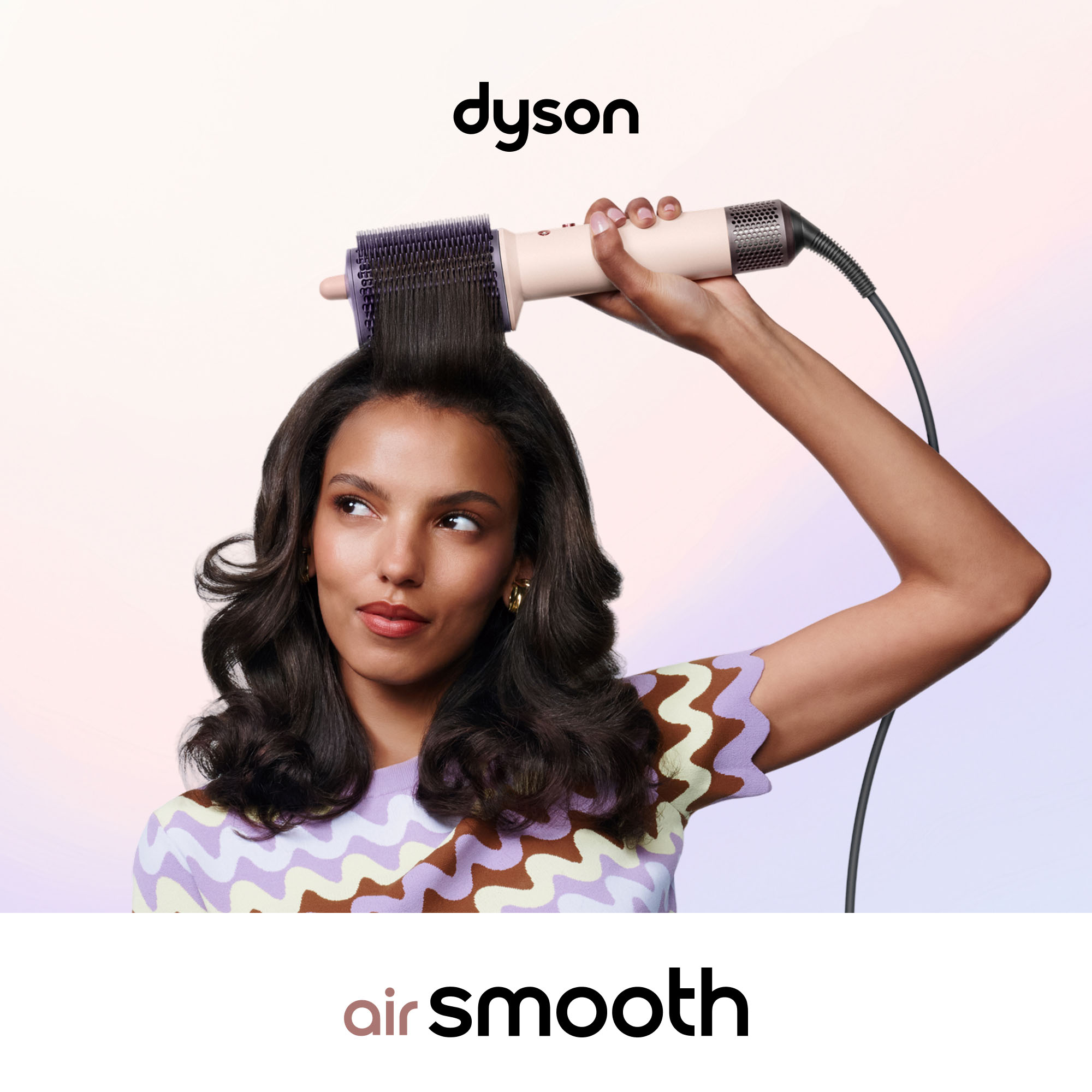 Eine Frau stylt ihr langes dunkles Haar mit einem Dyson Air-Stylinggerät vor hellem Hintergrund.