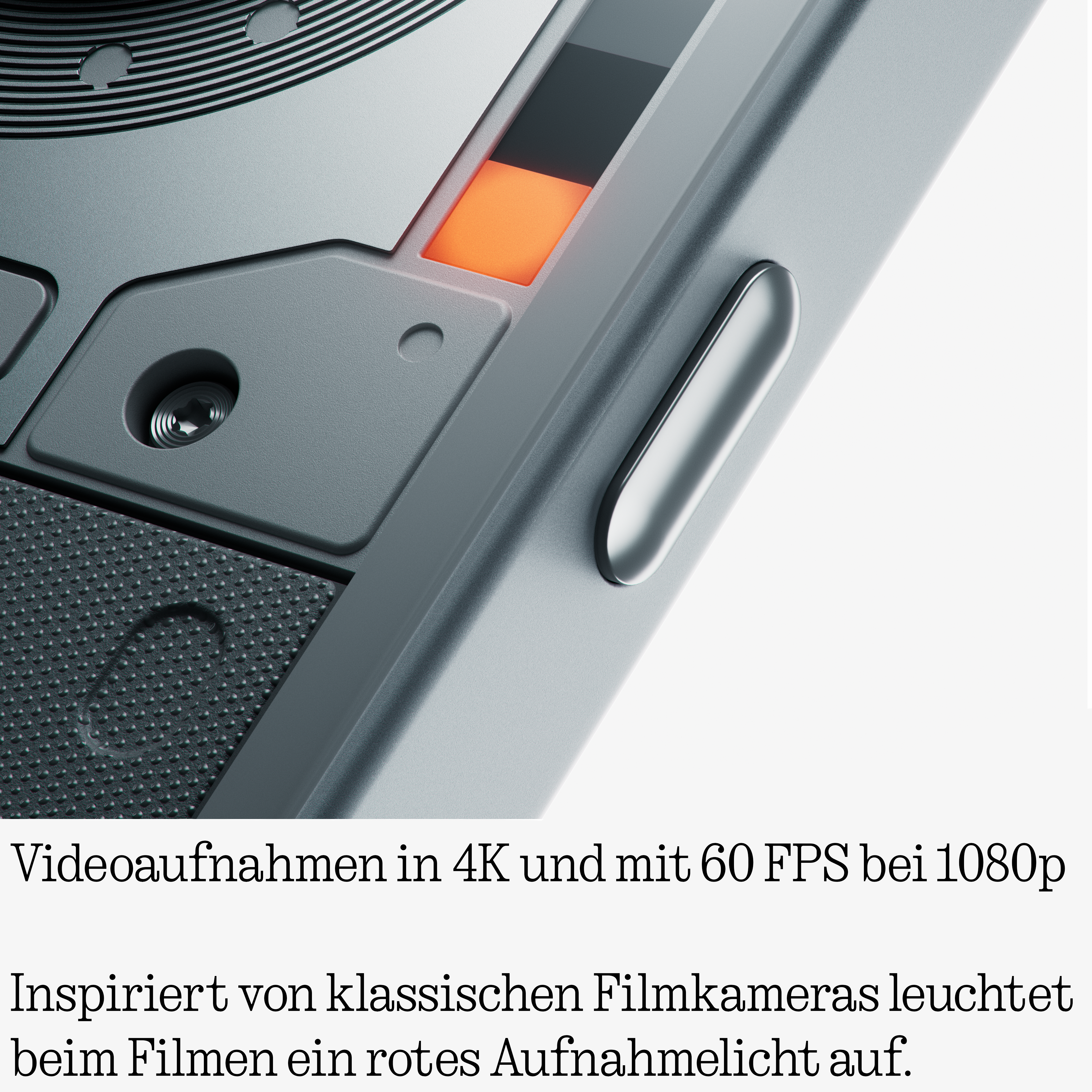 Nahaufnahme einer grauen Kamera mit orangem Licht, geriffeltem Griff und Text in deutscher Sprache unten.