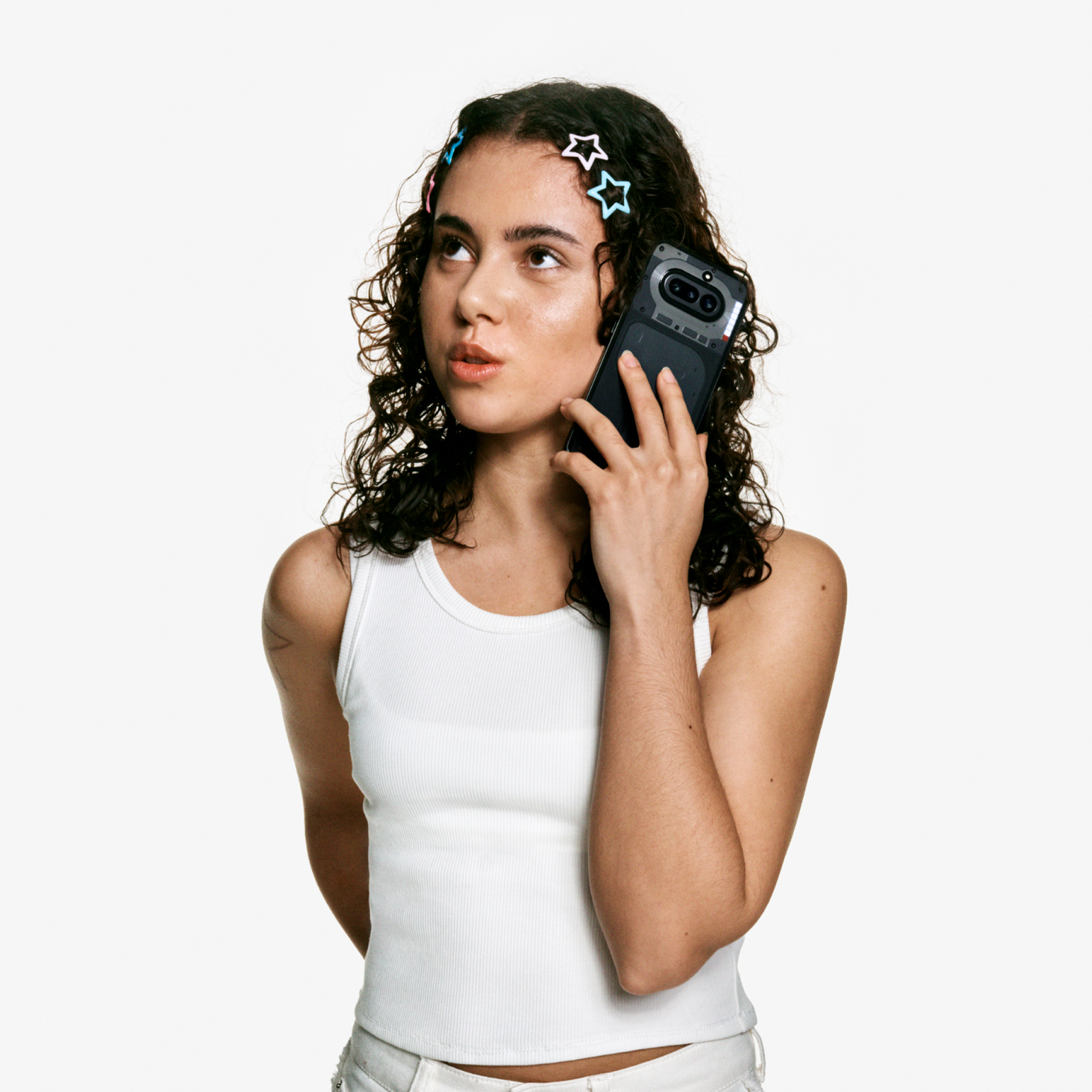 Eine Frau mit dunklen Locken und sternenbesetzten Haarspangen hält ein Smartphone ans Ohr und blickt nach oben.