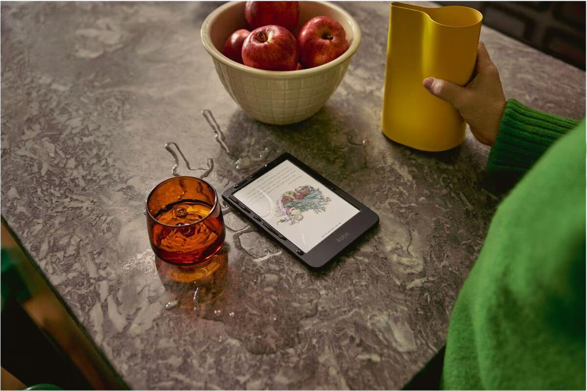 Ein E-Reader liegt neben einem Glas Wasser und einer Schüssel mit Äpfeln auf einer Steinarbeitsplatte.