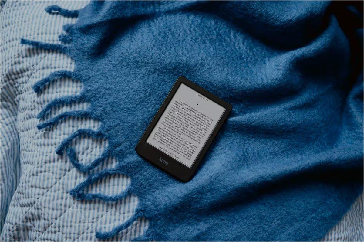 Ein Kobo-E-Reader mit Text liegt auf einer blauen Kuscheldecke und einem blau-weißen Laken.