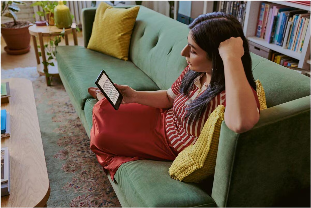 Eine Frau liest auf einem grünen Samtsofa mit gelben Kissen ein E-Reader.