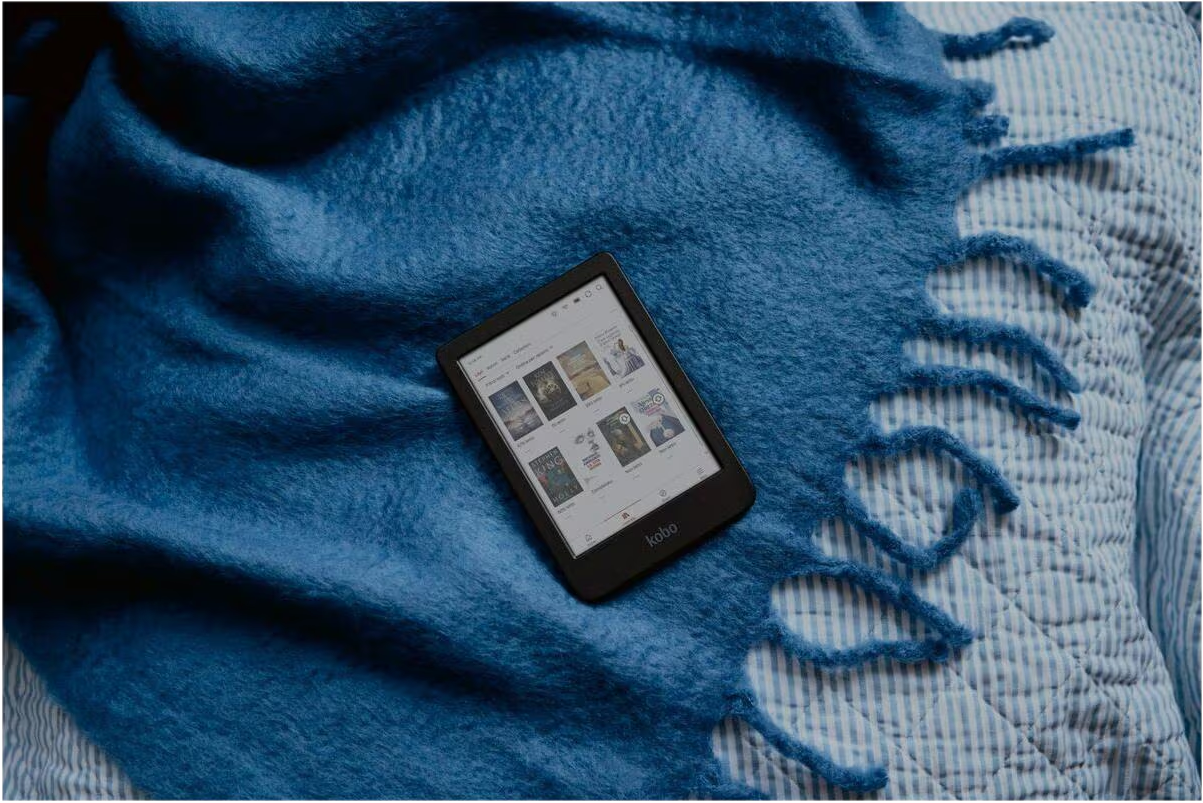 Ein schwarzer E-Reader liegt auf einer blauen Flauschdecke über blau-weiß gestreiften Laken.