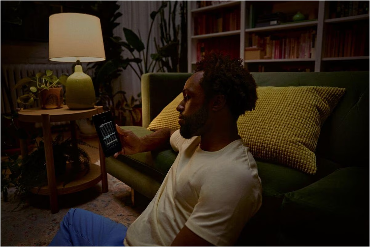 Ein Mann sitzt abends auf dem Boden vor einem grünen Sofa und liest auf einem E-Reader.