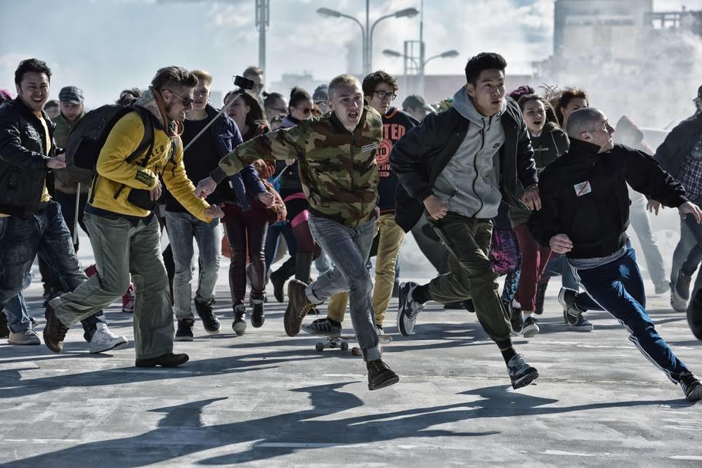 Eine diverse Gruppe von Menschen rennt in Eile über eine sonnige Straße, ein skateboarding Person im Hintergrund.