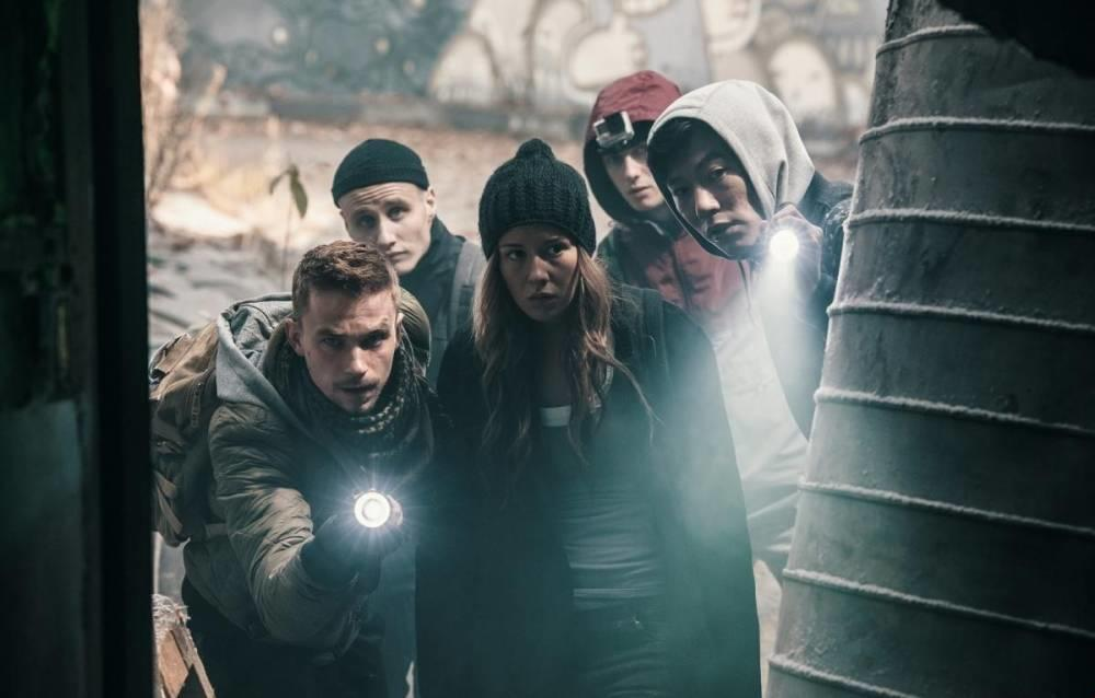 Fünf Personen mit Taschenlampen blicken aus einer dunklen Ruine, beleuchtet von starkem Schein.