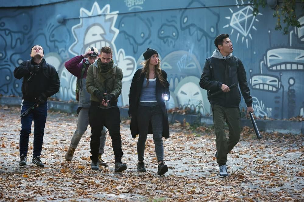 Fünf Personen wandern auf einem herbstlichen Weg vor einer graffiti-bedeckten Wand.
