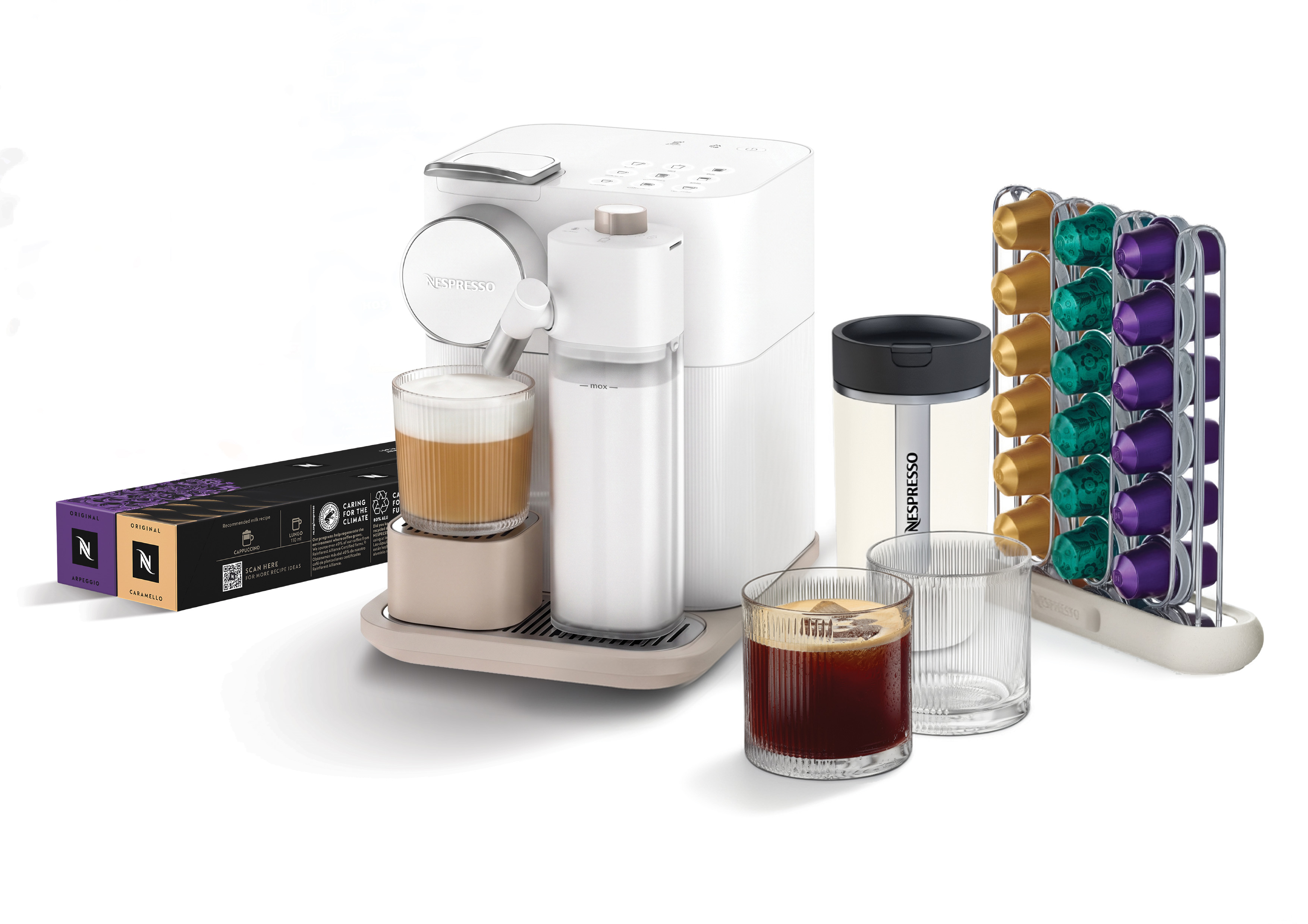 Beyaz arkaplanda süt hazneli, fincanlı, kapsül standlı ve kahve kutulu beyaz Nespresso kahve makinesi.