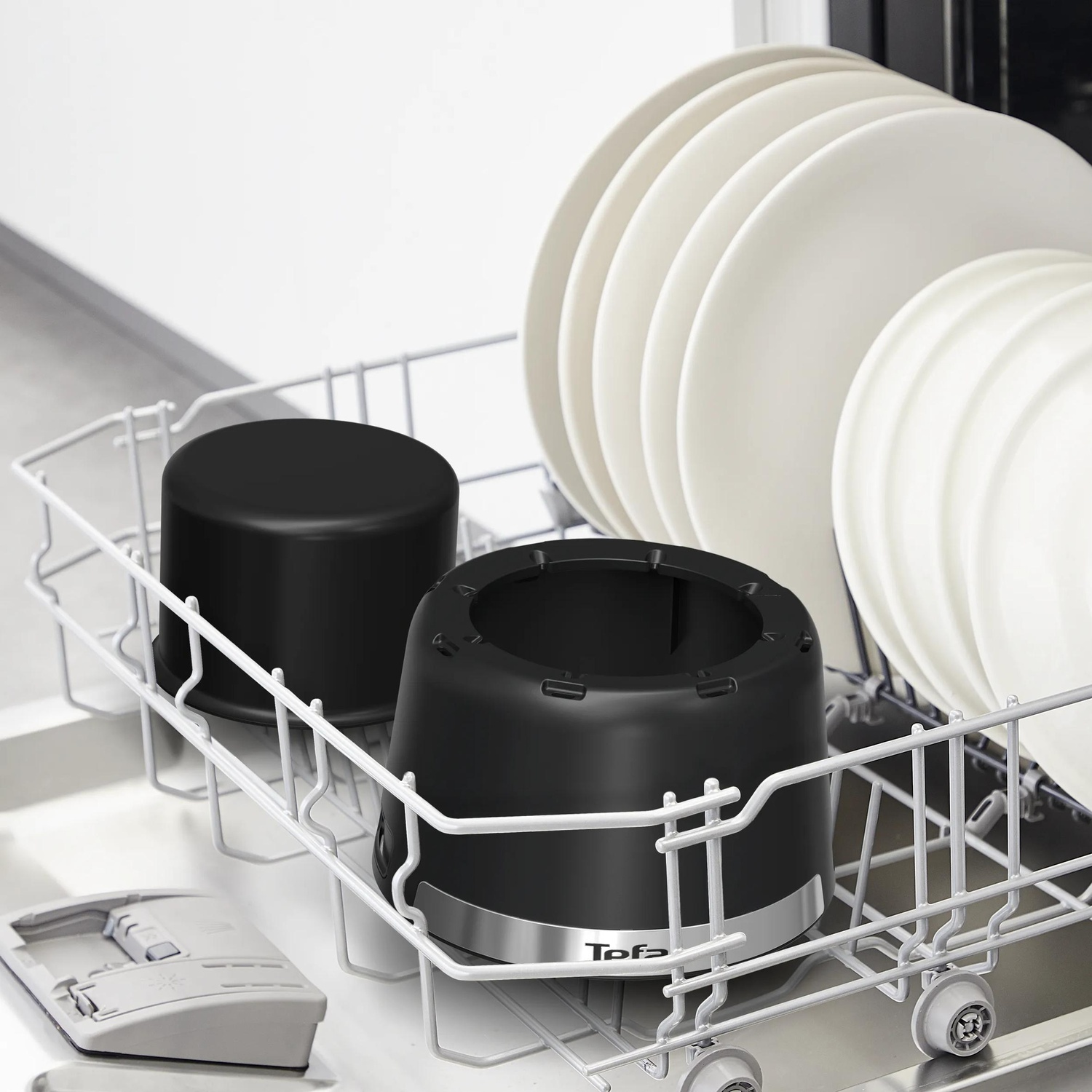 A dishwasher rack filled with white plates, a black container, and a black base with the Tefal logo.