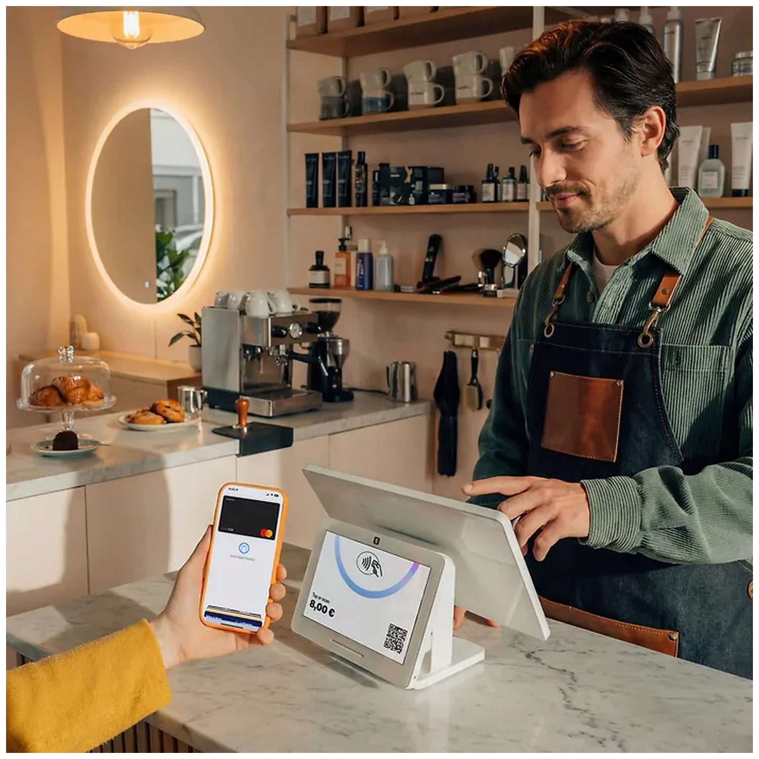 A barista operates a POS terminal while a customer pays with a smartphone.