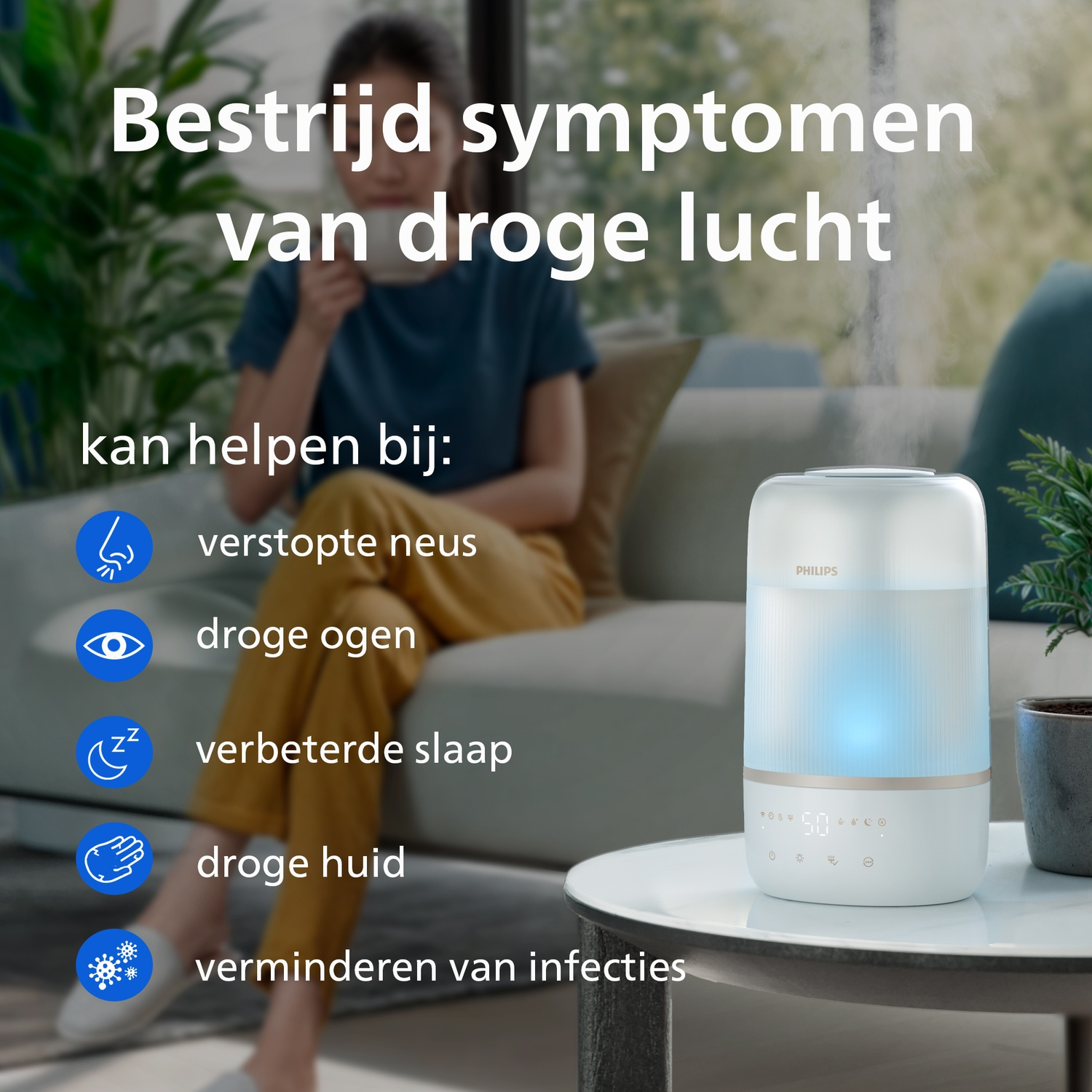A white Philips humidifier on a table emitting mist, with a woman sitting on a sofa in a blurred background.