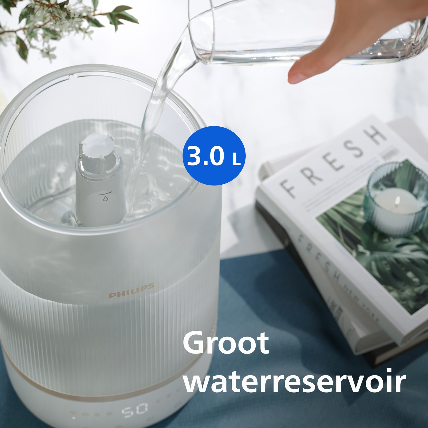 Water being poured into a Philips 3.0L water reservoir next to a book and candle.