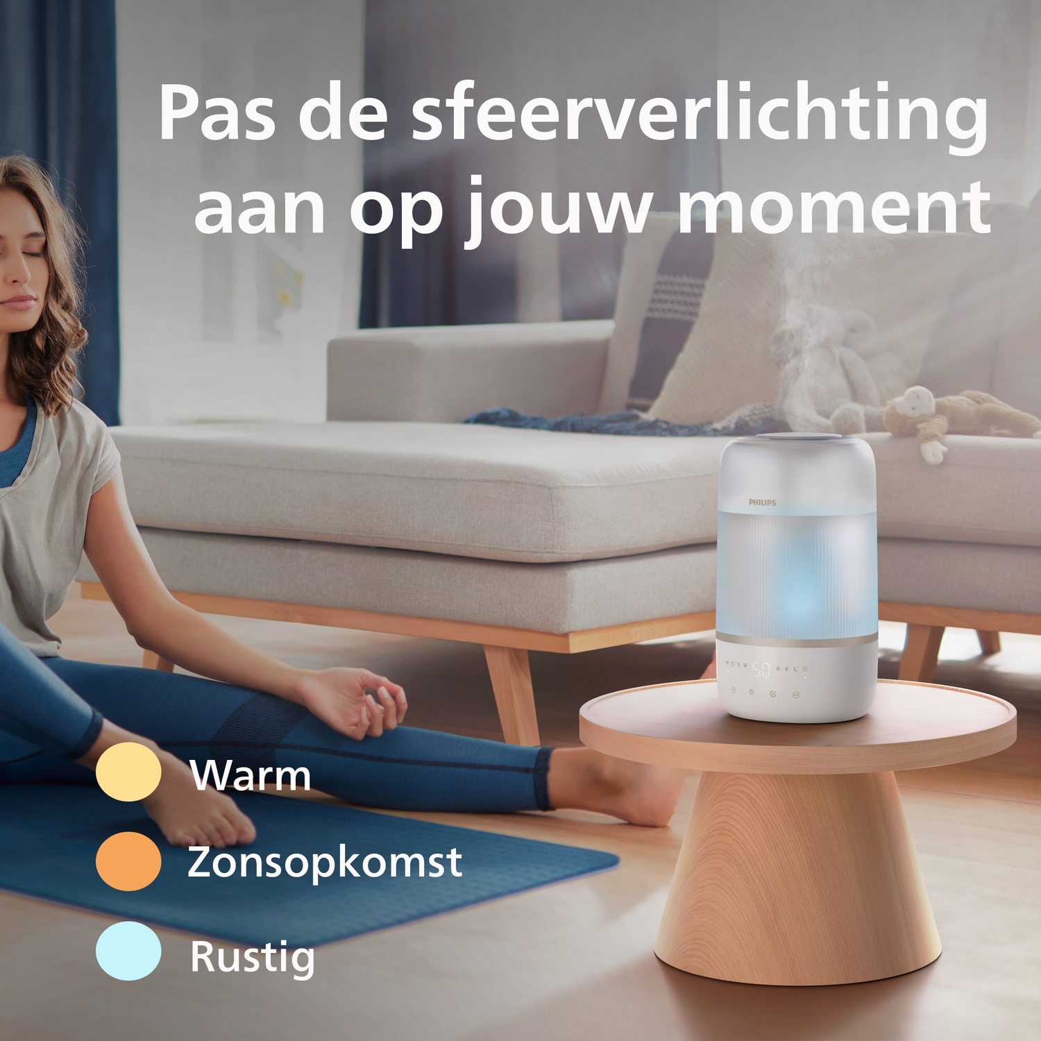 Woman meditating on a blue mat next to a Philips diffuser on a small wooden table in a living room.