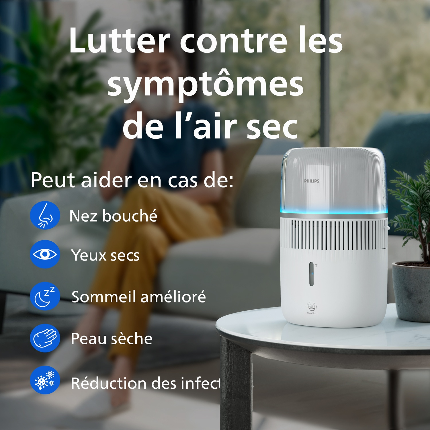 Un humidificateur Philips blanc sur une table dans un salon, avec une femme assise sur un canapé en arrière-plan.