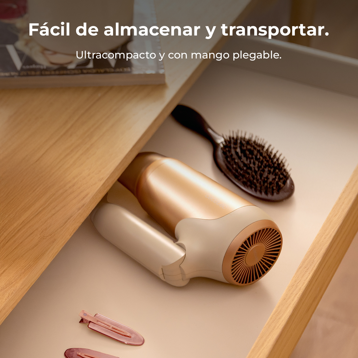 Secador de pelo plegable en tonos beige y dorado y un cepillo en un cajón de madera abierto con pinzas.