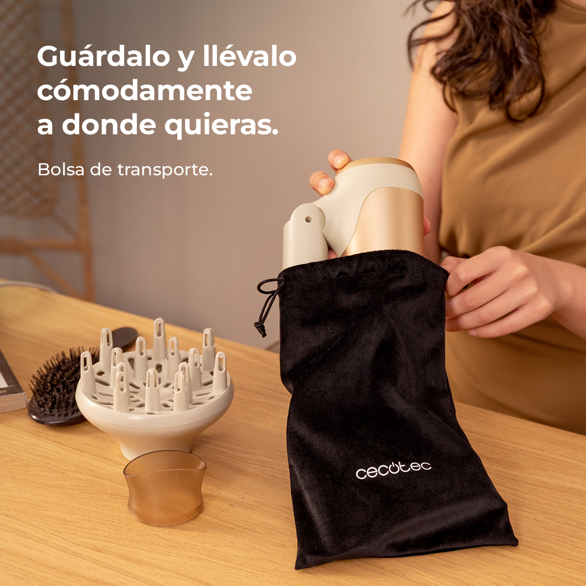Una mujer guarda un secador dorado en una bolsa negra sobre una mesa de madera.