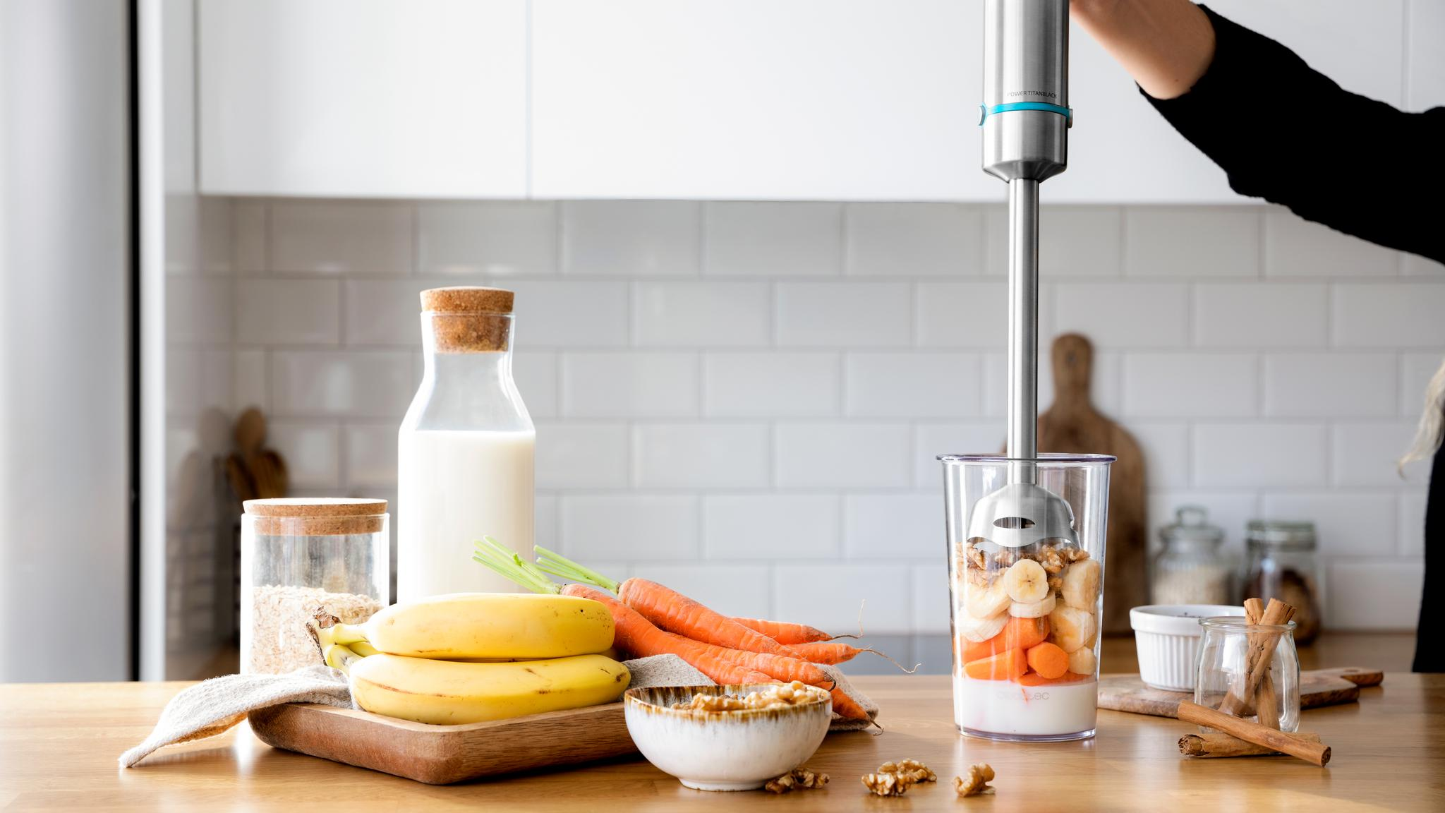 Persona batiendo plátanos, zanahorias, nueces y leche en un vaso.