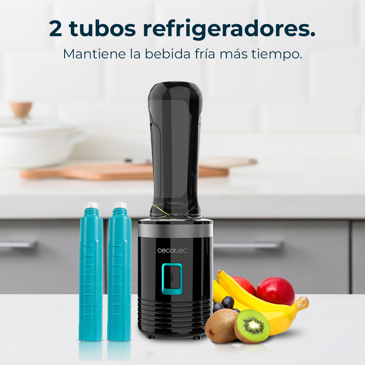 Batidora negra con dos tubos refrigerantes azules y frutas frescas sobre una encimera de cocina.