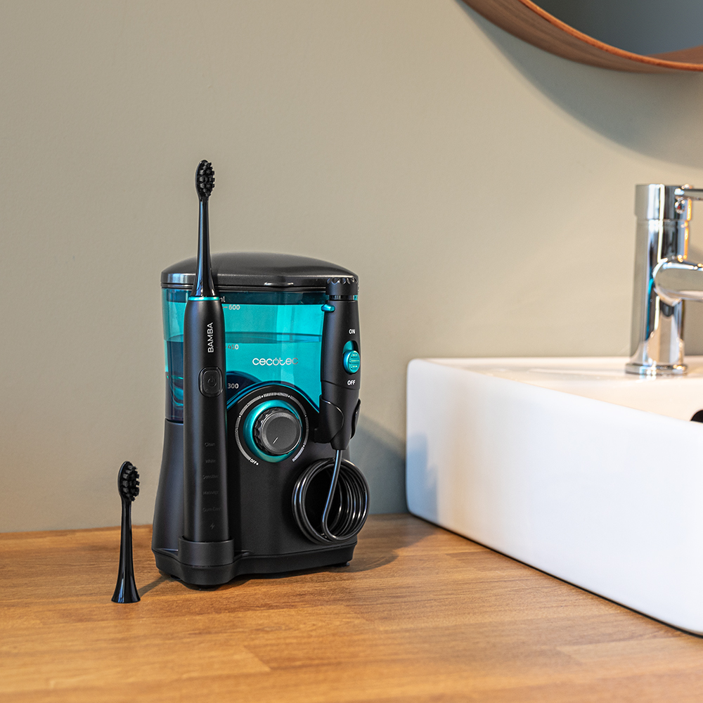 Un cepillo de dientes eléctrico negro y un irrigador bucal en una encimera de madera junto a un lavabo blanco.