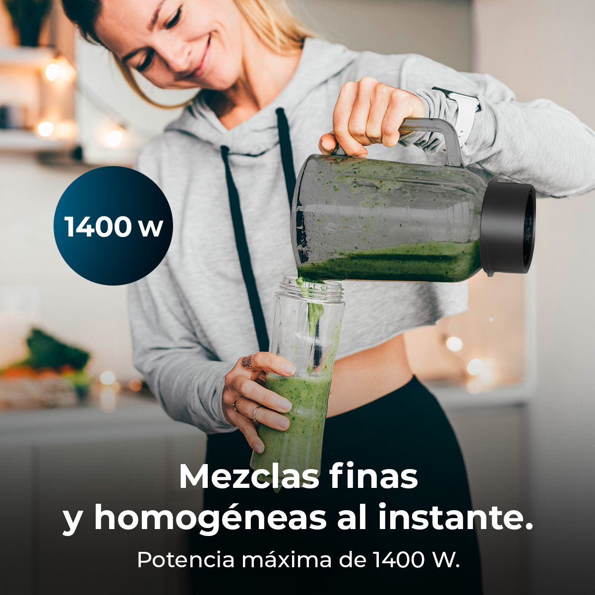 Una mujer con ropa gris vierte un batido verde de una licuadora en una botella pequeña.