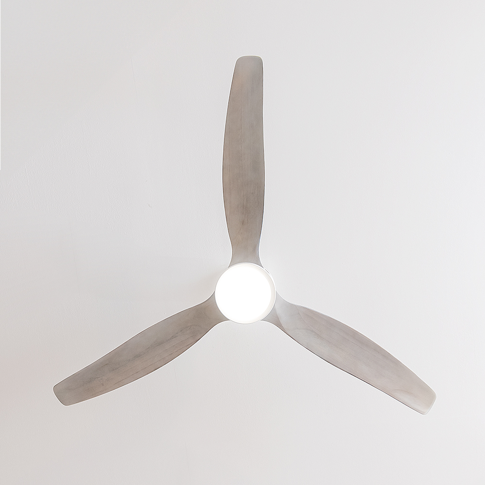 Un ventilador de techo blanco con tres aspas de madera y luz redonda central, montado en un techo blanco.