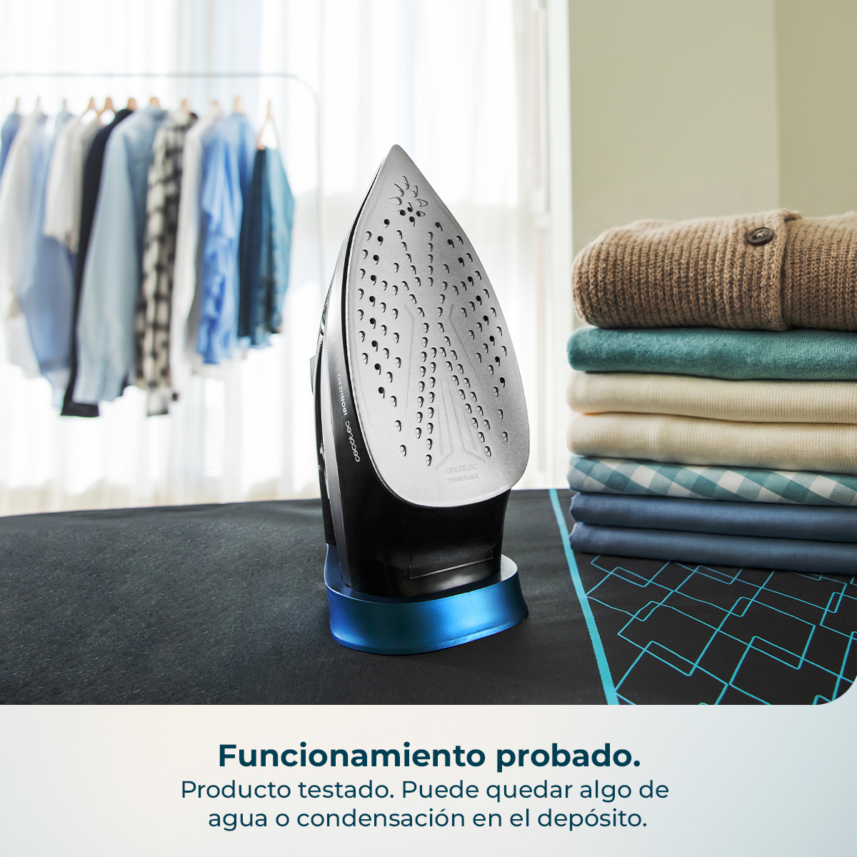 Una plancha de vapor se encuentra sobre una tabla de planchar junto a ropa doblada.