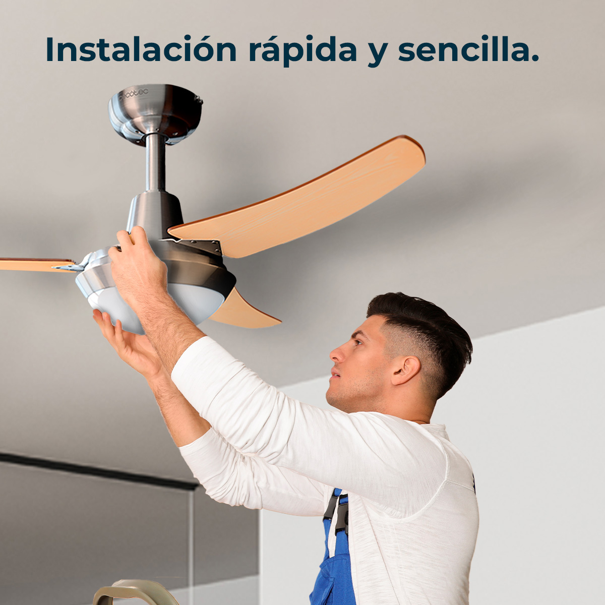 Un hombre con mono azul está instalando un ventilador de techo con aspas de madera.