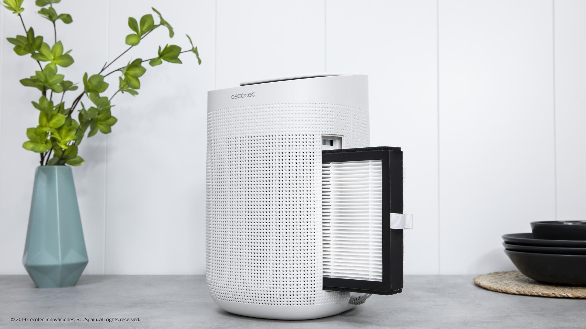 Un purificador de aire blanco con el filtro extraído está en una mesa contra una pared blanca.