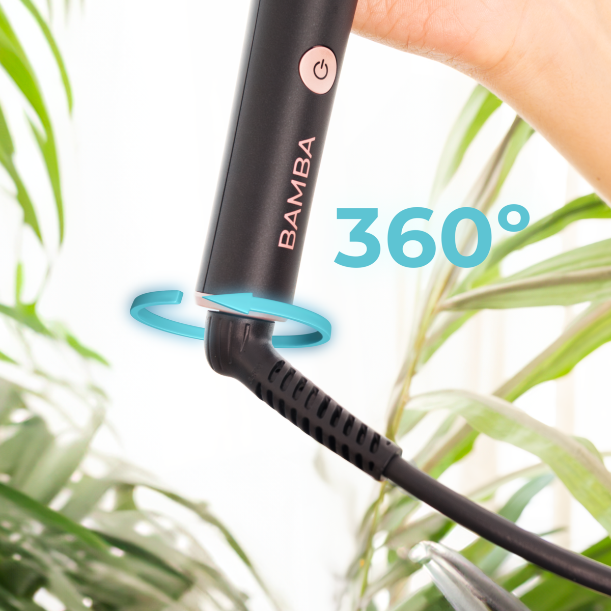 Mano sostiene una plancha Bamba con un cable giratorio de 360 grados ante plantas verdes.